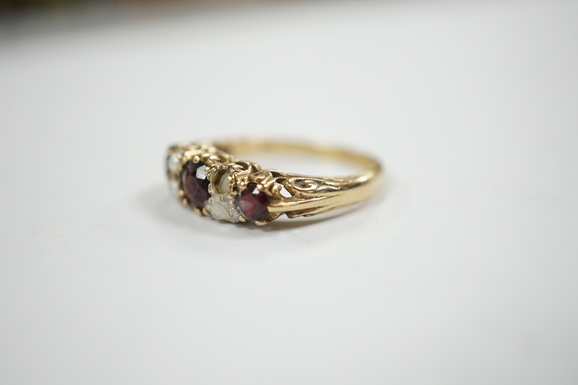 A modern 9ct gold, three stone garnet and four stone split pearl set half hoop ring (two pearls missing), size S/T, gross weight 3.8 grams.